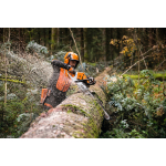 A person in orange protective gear uses a chainsaw to cut through a large moss-covered log in a forest.