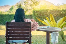 Back view of woman drink tea or coffee at summer garden. Carefree woman breathing fresh air relaxing drinking coffee in garden at home. Asian lady resting in a garden having hot coffee in afternoon.