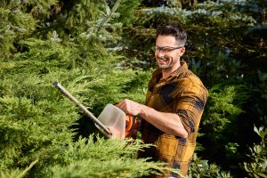 Man trimming bush in his garden with a hedge trimmer wearing protective glasses