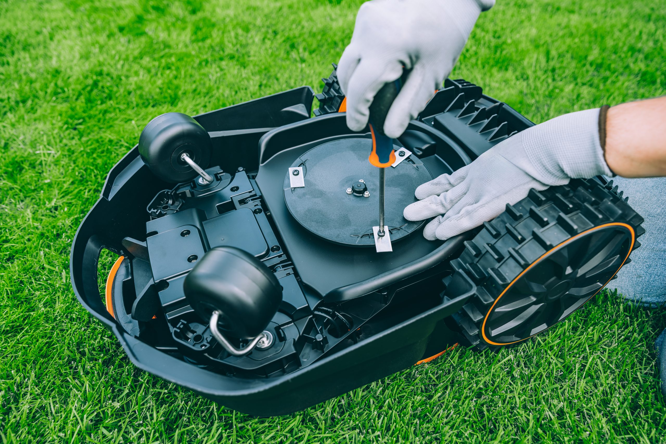 A man changes the blades of a robotic lawn mower. Lawn Mower Maintenance at Home Workshop With Tools on a Sunny Day