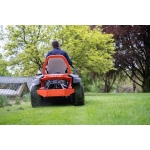 A person rides an orange Ariens zero-turn mower away from the camera across a garden lawn with trees in the background.