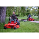 Two people ride orange Ariens zero-turn mowers across a grassy park with trees in the background.