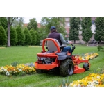 A person rides an orange Ariens zero-turn mower along a flower bed in a park setting.