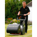 A man pushes a black Allett cylinder mower across a lawn in a garden with flower beds in the background.