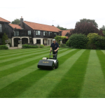 A man pushes a black Allett cylinder mower to create striped patterns on the lawn of a grand house.