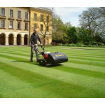 A man pushes an Allett cylinder mower across a striped lawn in front of a grand stone building.