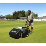 A man pushes a black Allett cylinder mower across a manicured sports field under a clear blue sky.