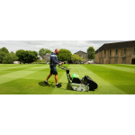 A man pushes a cylinder mower across a large striped lawn in front of grand stone buildings.