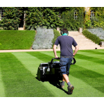 A groundsman pushes a cylinder mower creating stripes before a stone building.