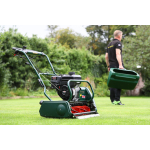 A green cylinder mower on a lawn while a man walks away with its grass collector.