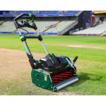 A green and black Allett cylinder mower stands on the grass of a cricket ground with empty stands in the background.