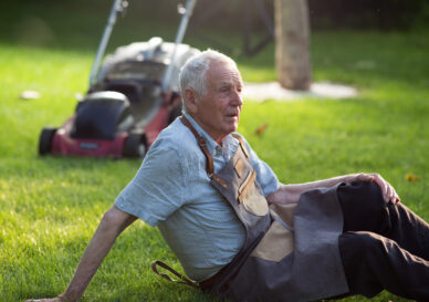 Senior man resting on lawn after mowing grass in courtyard