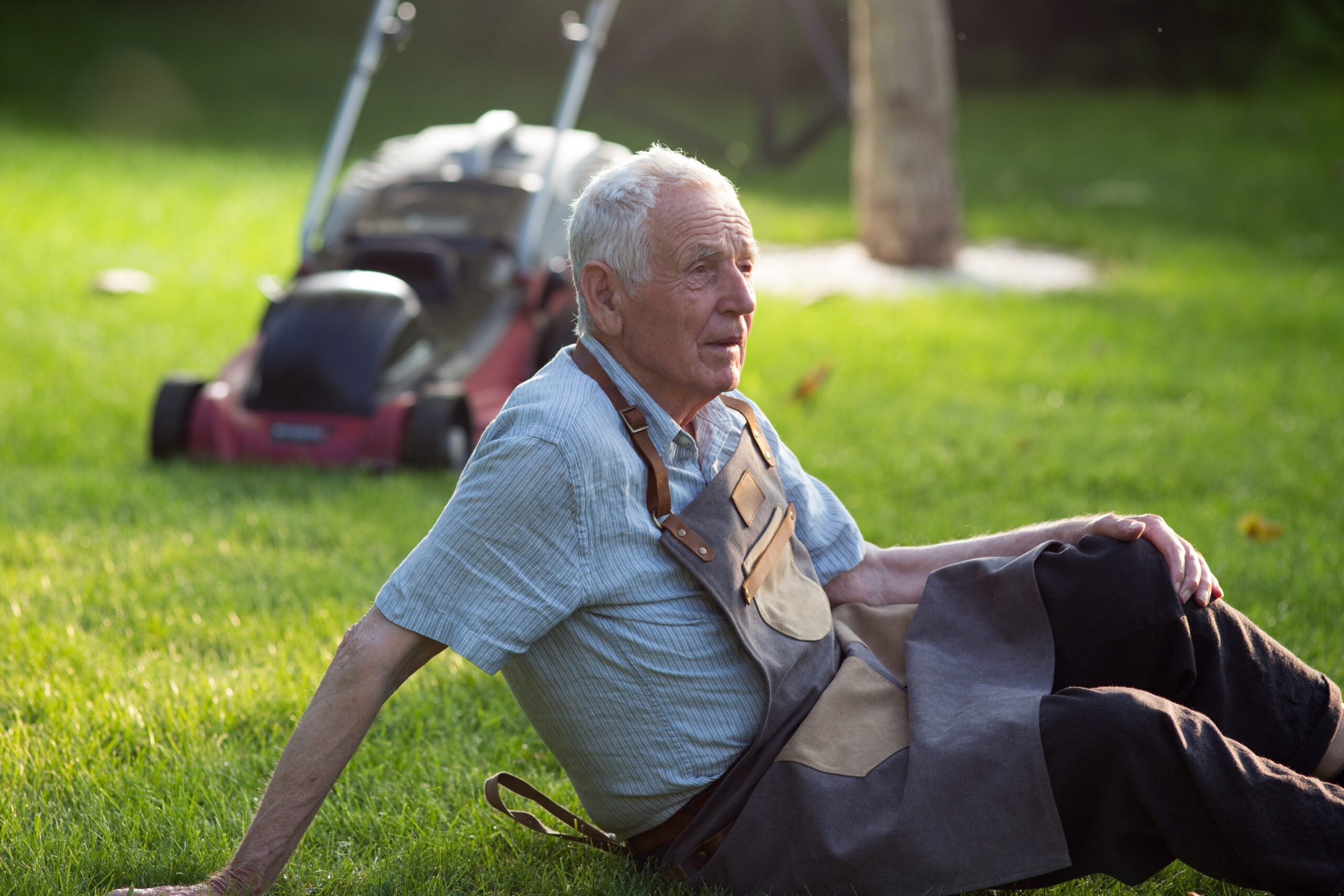 Senior man resting on lawn after mowing grass in courtyard