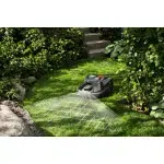 A robotic lawn mower operating on a well-maintained garden lawn with surrounding greenery.